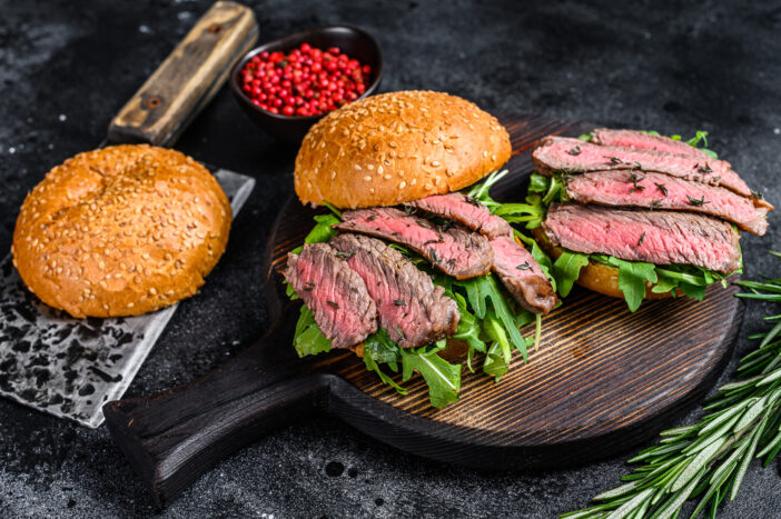 Traditional sliced cold cuts roast beef burger with onion, gherkin, arugula and spinach. Black background. Top view.