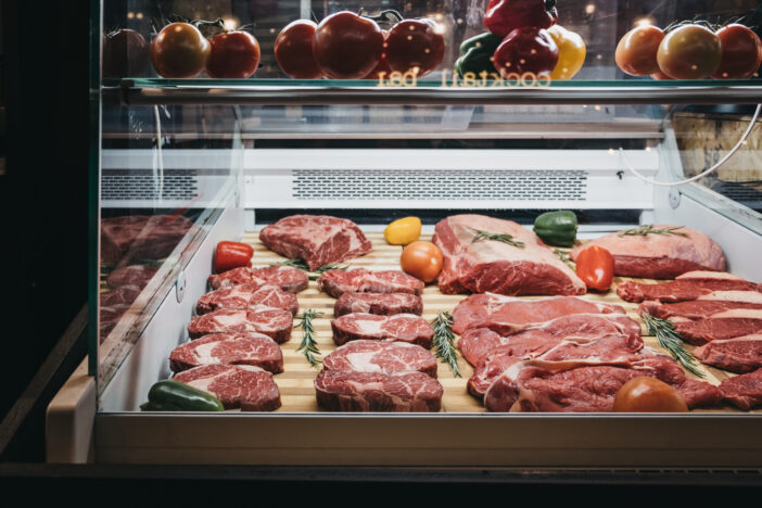 Variety of fresh raw steaks on display in a fridge at butcher's shop at the market.