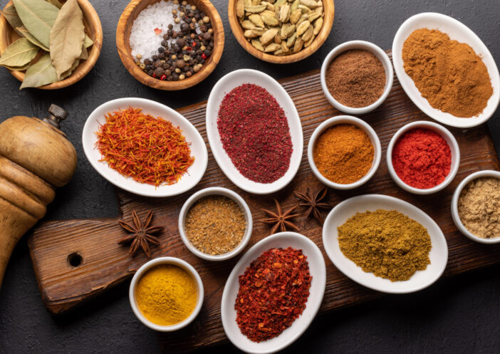 Various dried spices in small bowls on wooden board