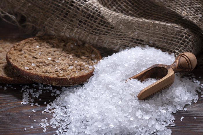 White sea salt for cooking food on a fired wooden table, natural spoon, bread and coarse bag