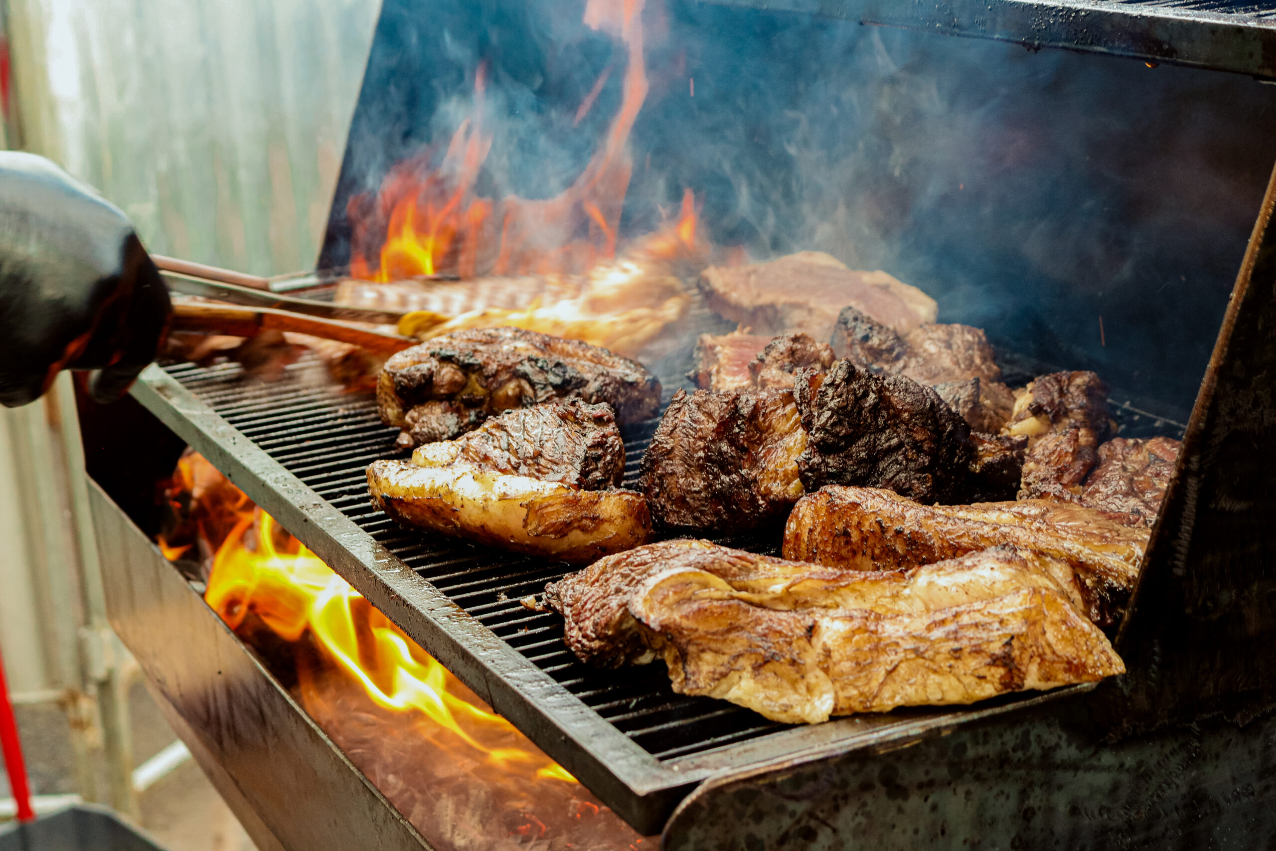 a barbecue with pieces of meat on fire and a hand taking a piece