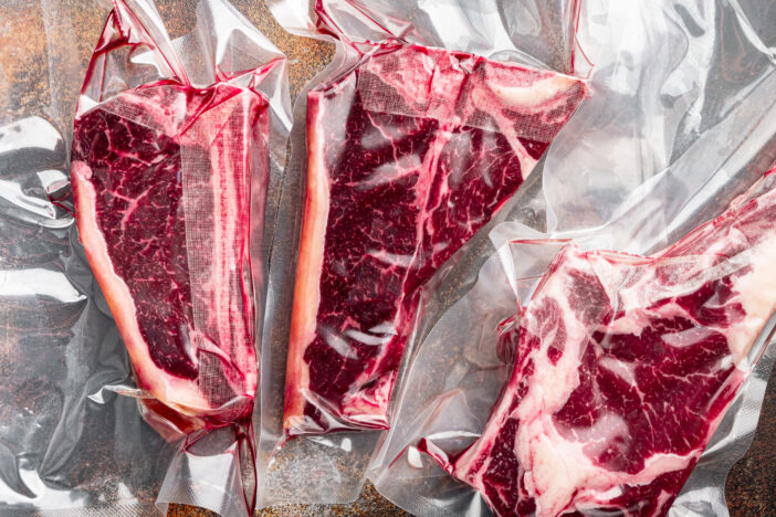 Dry aged steak in a vacuum. Meat products in plastic pack set, tomahawk, t bone and club steak cuts, on old dark rustic background, top view flat lay