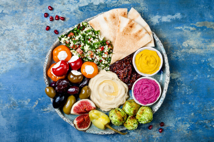 Middle Eastern meze platter with green falafel, pita, sun dried tomatoes, pumpkin and beet hummus, olives, stuffed peppers, tabbouleh, figs. Mediterranean appetizer party idea