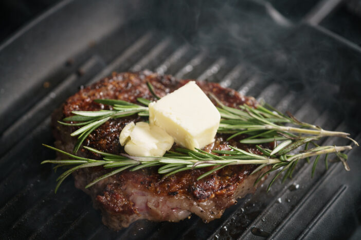 beef rib eye steak with rosemary on grill pan closeup, shallow focus