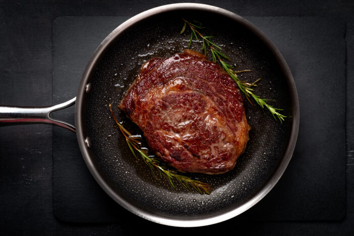 Grilled premium rib eye beef steak in the pan, cooking steak in the kitchen on a dark background, top view