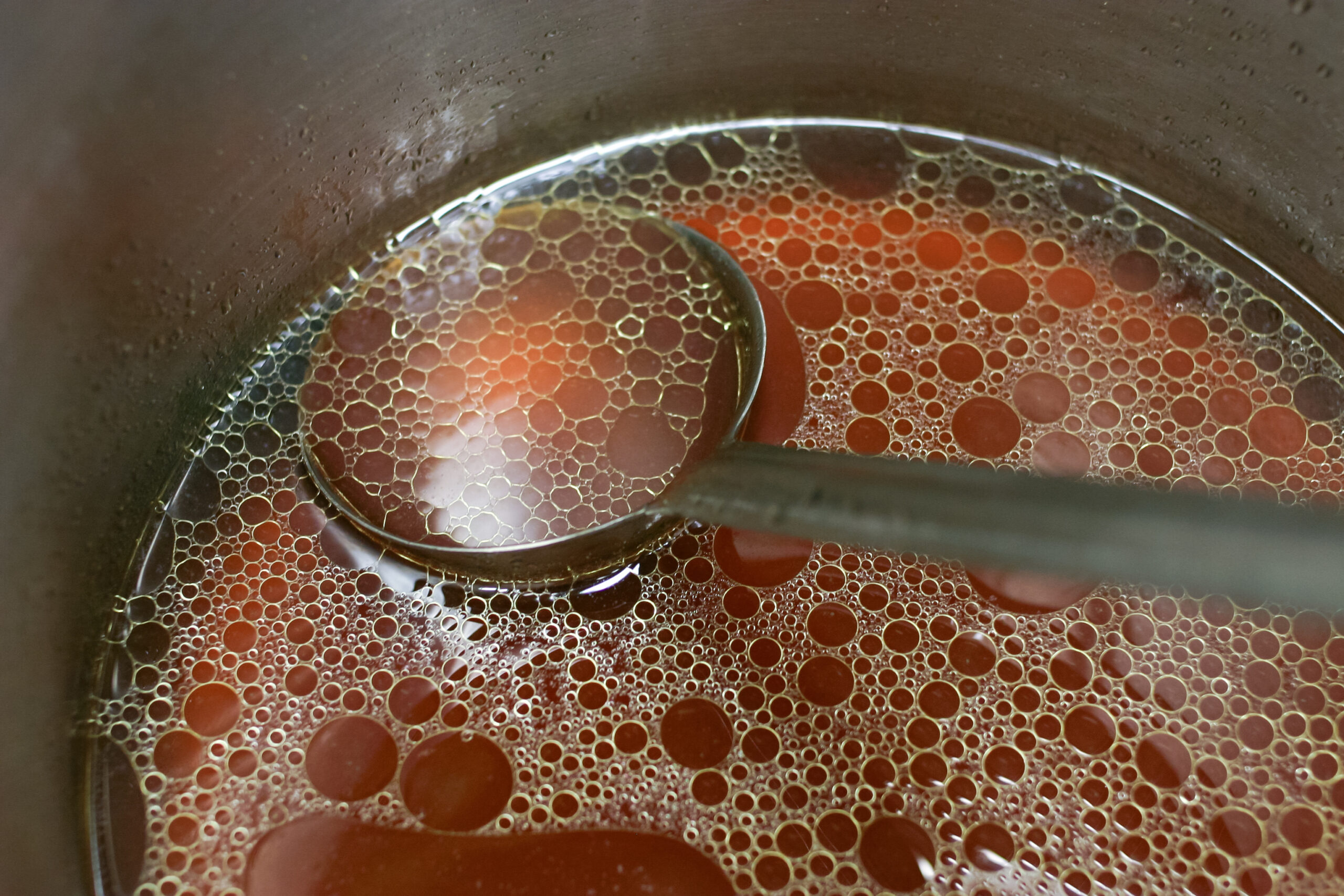 Rich meat stock in a pot of  with a ladle and fat floating on top