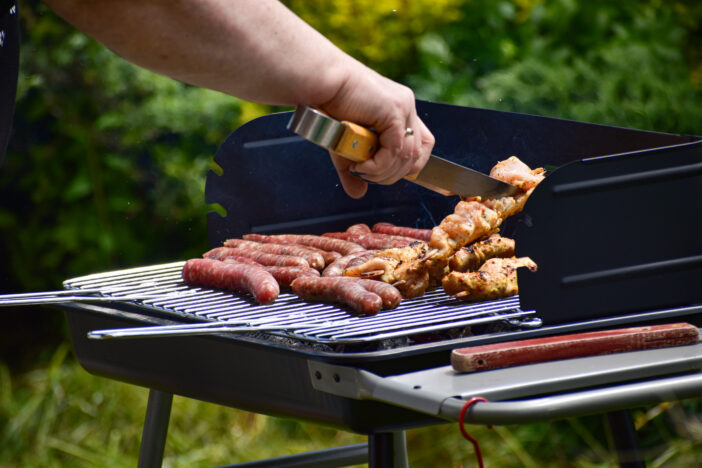 A female is grilling some saussages and meat on the grill