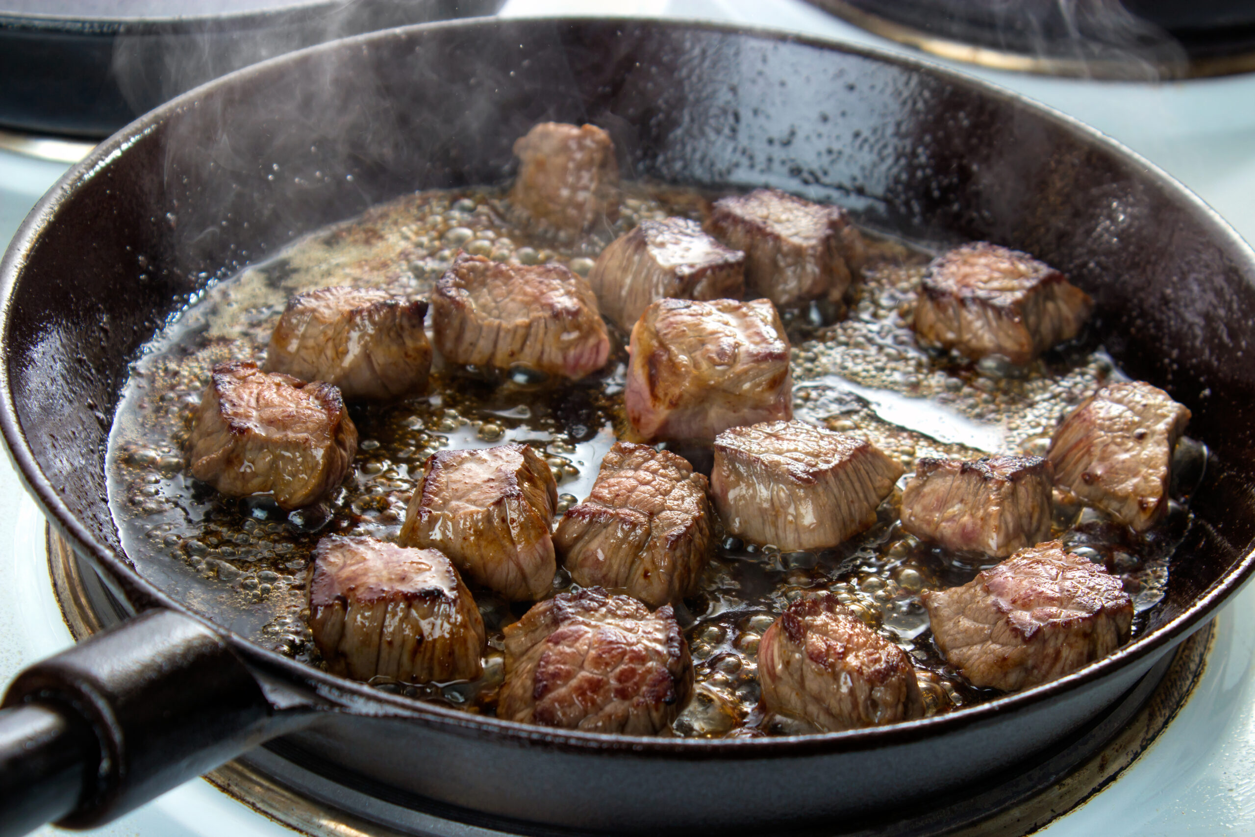 Frying beef bottom round roast cubes in cast iron skillet , meat flipped once