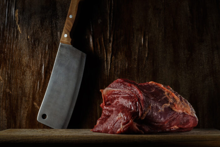piece of fresh raw beef tenderloin on a cutting board with a kitchen cleaver against an old wooden wall. artistic moody photo in rustic style with copy space