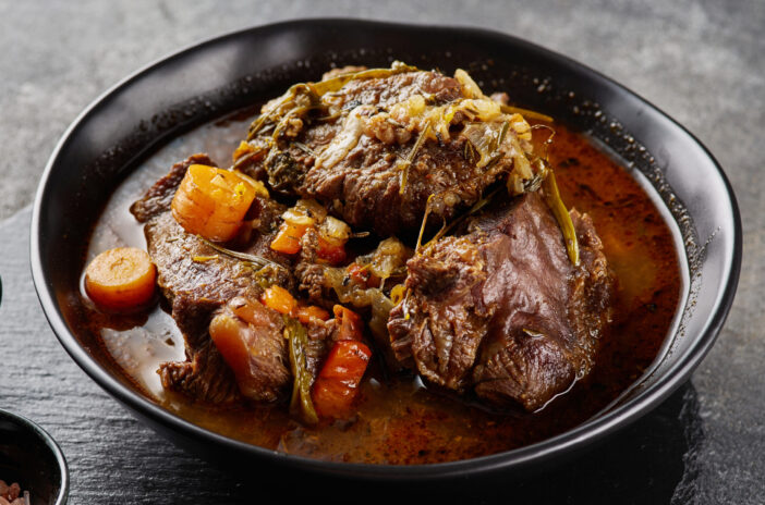 Traditional German braised beef cheeks in brown red wine sauce with herbs as closeup in black plate