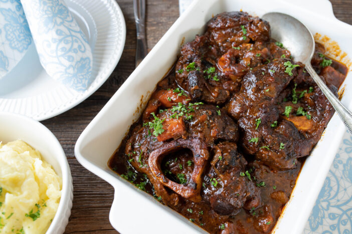 Deicious braised dish with beef shanks or leg slices. Cooked with a delicious brown sauce and vegetables. Served with mashed potatoes on rustic and wooden table background from above.