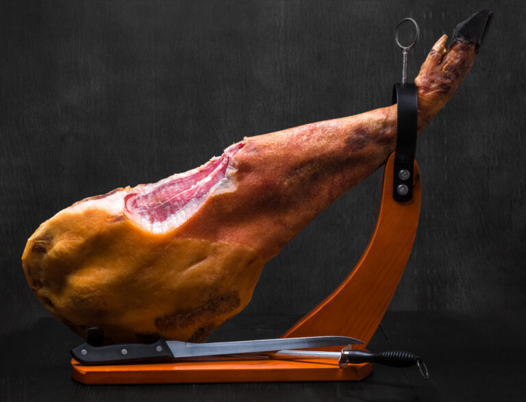 Whole jamon on a wooden stand on dark background. Ham