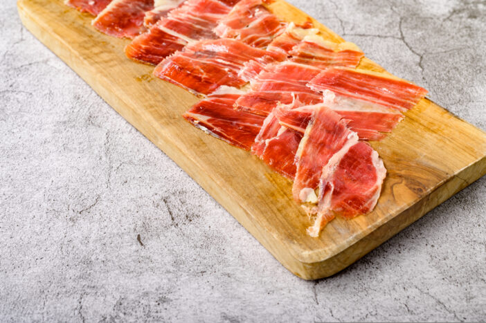 From above view of thin slices of delicious jamon served on wooden chopping board placed on gray surface