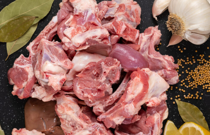 Fresh raw goat meat stew like cuts on black cutting board with spices (mustard seeds, garlic, lemon, and bay leaves).