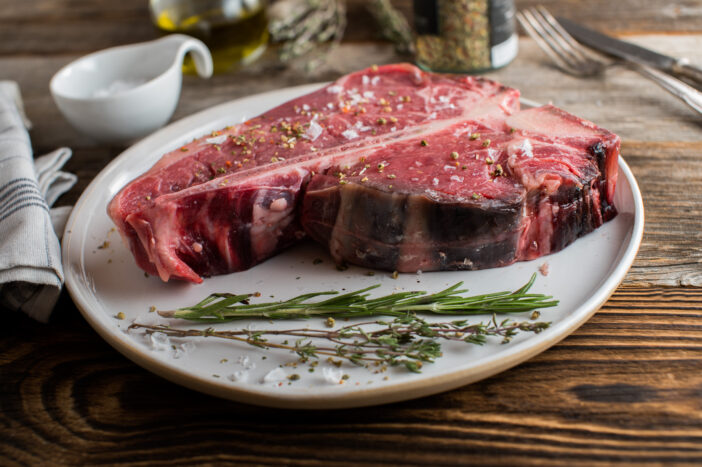 Organic and grass fed t-bone or porterhouse steak with salt and pepper seasoning served raw and uncooked on wooden table background