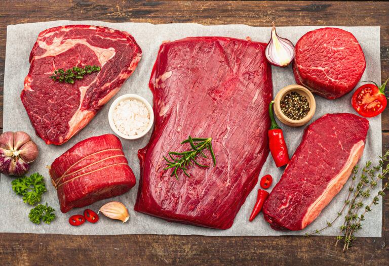 Set of various steaks with traditional spices and herbs. Fresh raw meat cuts includes ribeye, eye round, flank and striploin steaks. Old wooden background, flat lay, top view