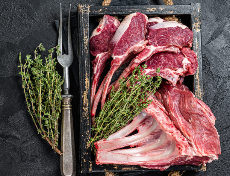 Uncooked Raw Rack and lamb, mutton rib chops  in a wooden tray. Black background. Top view. Copy space.