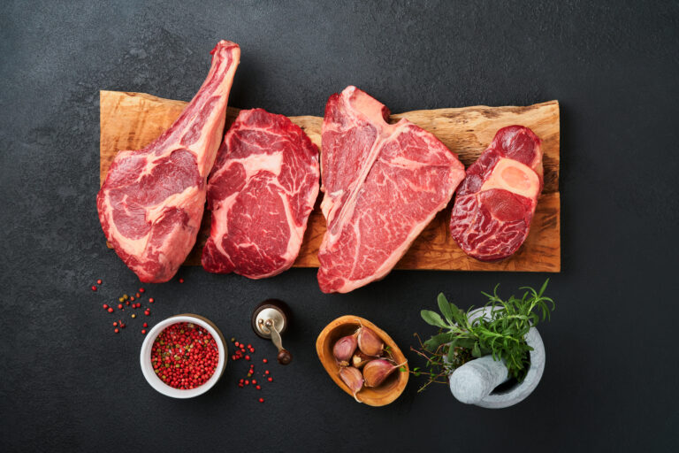 Raw prime steaks. Variety of fresh black angus prime meat steaks T-bone, New York, Ribeye, Striploin, Tomahawk cutting board on black or dark background. Set of various classic steaks. Top view.