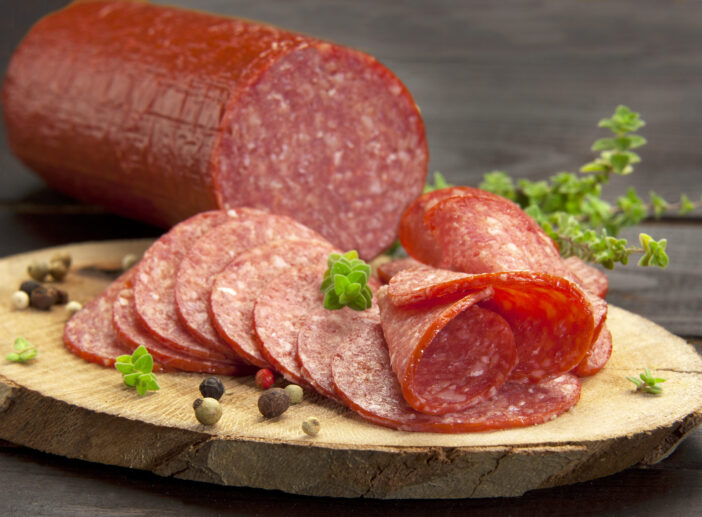 halved in slices turkey salami served on a slice of wood with thyme and ground pepper