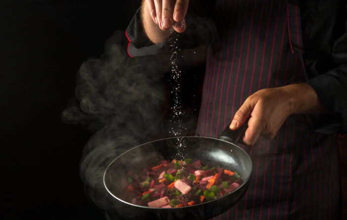 Cooking fresh vegetables. The chef adds salt to a steaming hot pan. Grande cuisine idea for a hotel with advertising space.