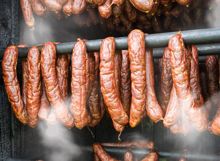 Closeup of hot smoky sausages from pork and beef meat hanging inside homemade smokery. Making tasty savoury charcuterie in smokehouse