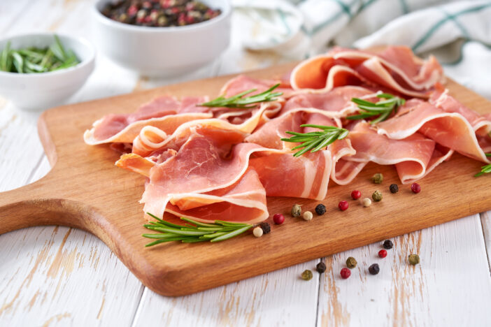 italian parma ham prosciutto with rosemary and pepper on a white wooden table, selective focus.