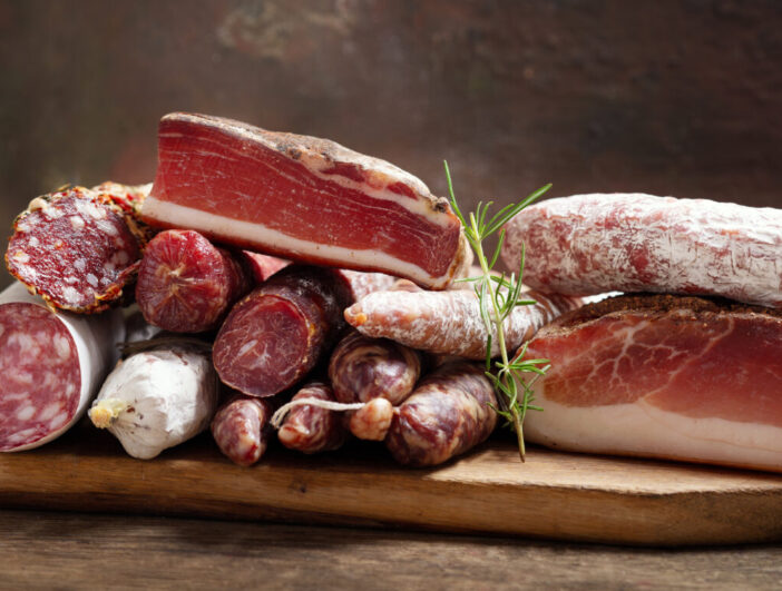 Italian food. Various kind types of salami, speck, sausages, parmesan cheese, green olives, basil and fresh tomatoes on a wooden table