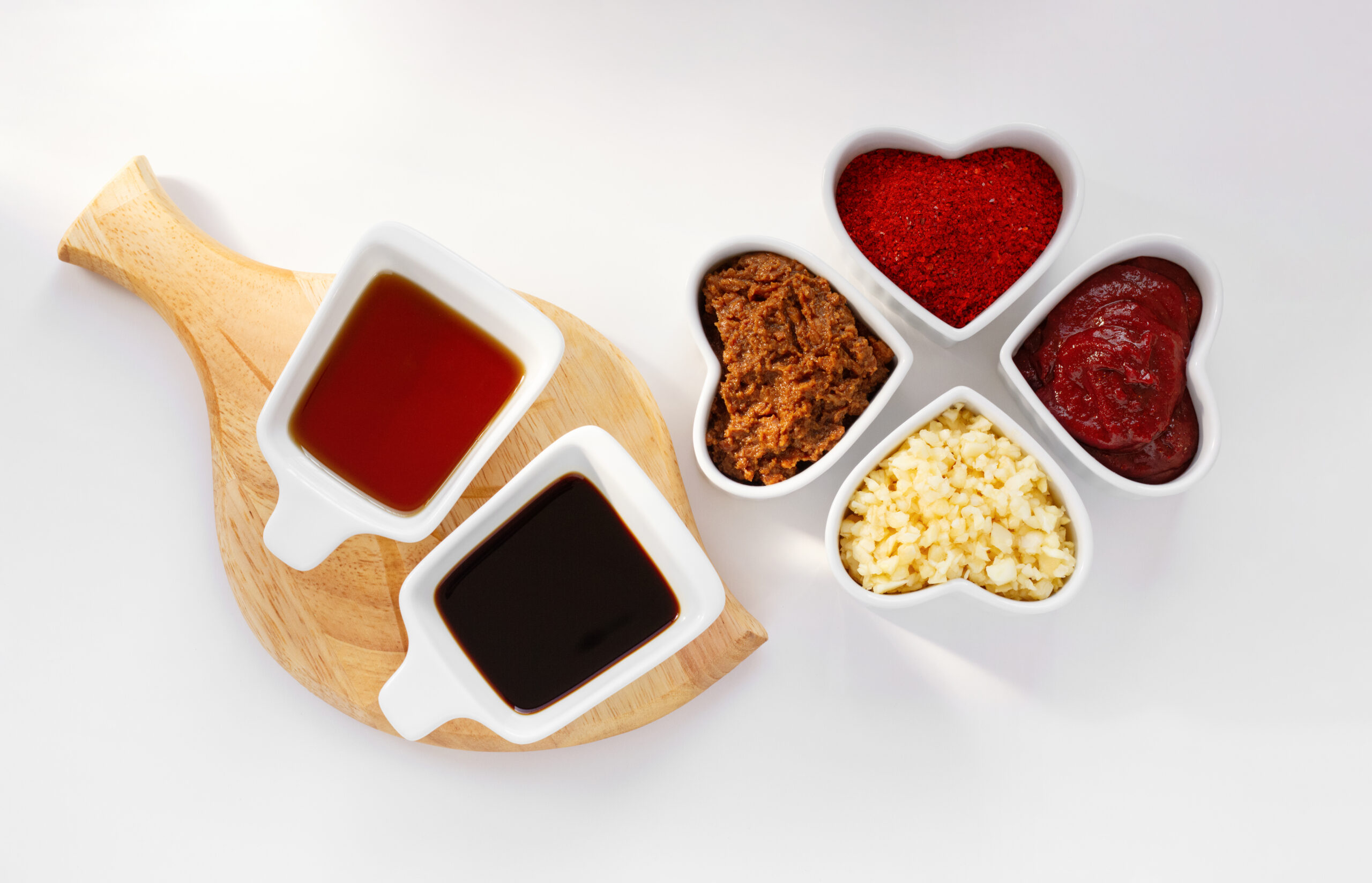 Traditional Korean sauce set in the heart shape bowl. Sesame oil, soy sauce, soybean paste, red pepper powder, red pepper paste and minced garlic isolated on white background.