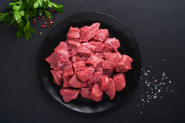 Raw chopped beef meat. Raw organic meat beef or lamb, spices, herbs on black plate on dark grey concrete background. Goulash. Raw uncooked meat. Meat with blood. Top view with copy space.