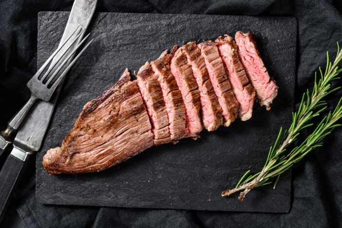 Grill Restaurant Beef Menu - Flank Steak on a black stone Board. Black background. Top view.