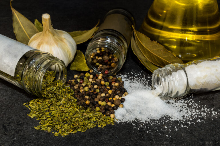 Different types and kinds of food spices falling off from their glass containers into a dark surface.