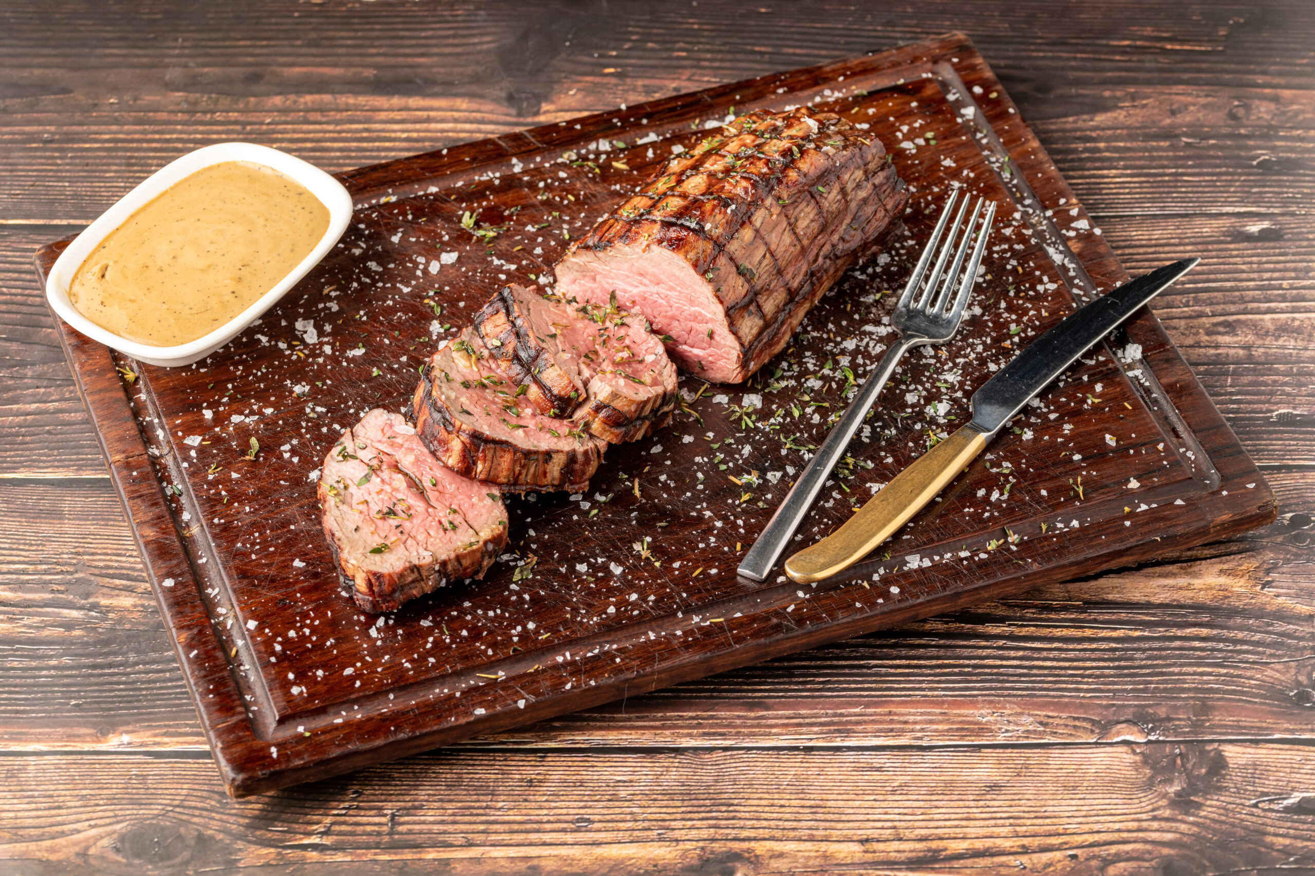 Sliced grilled beef tenderloin seasoned with salt, rosemary and thyme on a wooden cutting board