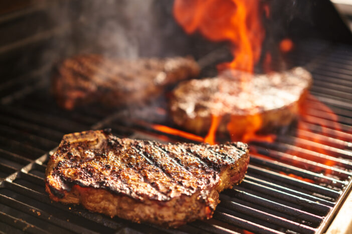 steaks cooking over flaming grill