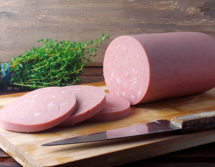 piece of whole raw pork bologna on cutting board with some slices. Italian food