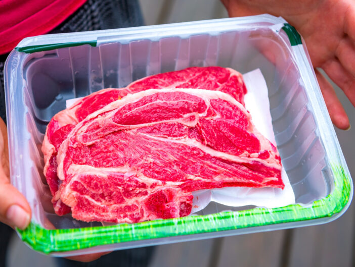 Red raw lamb meat shoulder chops from New Zealand packaged storebought with woman holding open plastic container showing