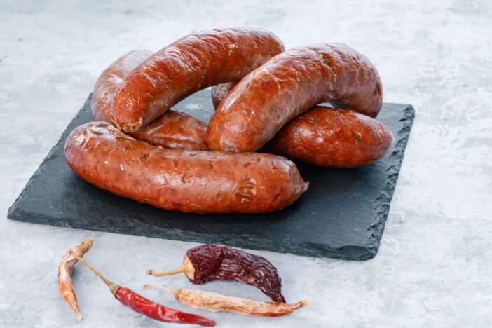 On a concrete table sits a small square black slate bearing a serving of roasted Nduja sausage.