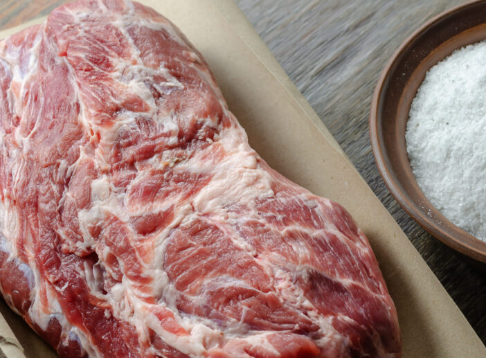 Homemade Capicola (coppa). Dry-cured pork loin step-by-step recipe. Large Whole piece of raw pork meat on paper. Clay bowl with salt. Preparation for pickling meat. Traditional Italian cuisine.