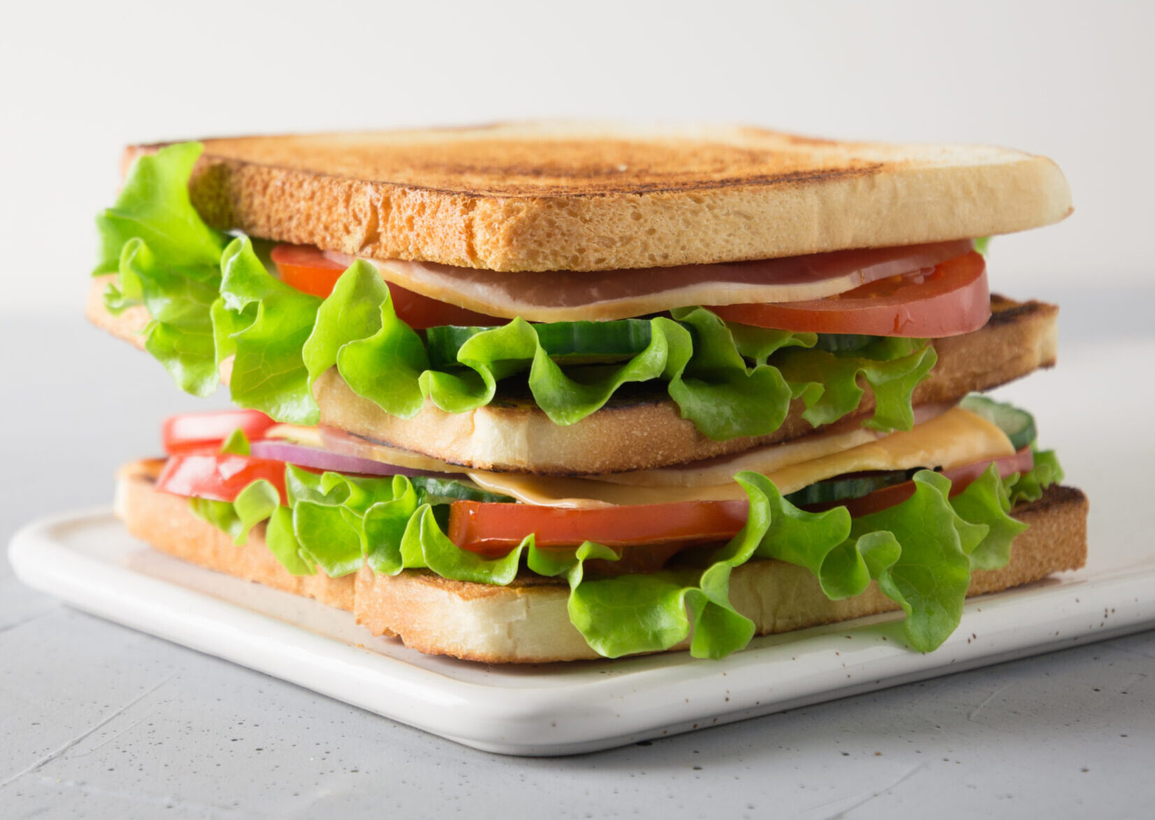 Sandwich with white toast bread, bacon, tomato, onion, salad, cheese on light background. Space for text