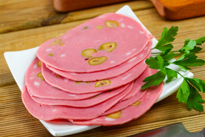 Close-up of sliced mortadela sausage with olives at wooden background