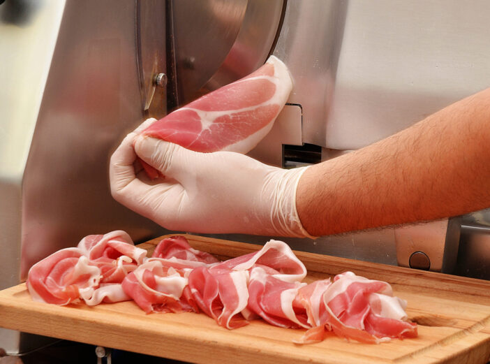 slicing prosciuto ham with industrial slicer machine.