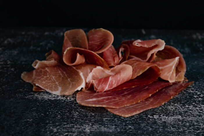 Pieces of pork meat on a black background. Italian prosciutto on a dark background. Selective focus. Spanish jamon