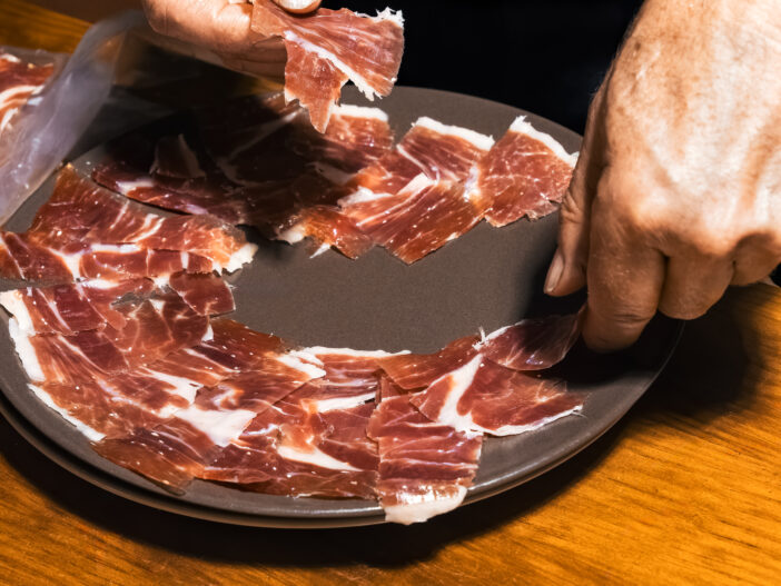 Expert hands artfully arrange thin slices of jamon on a plate.