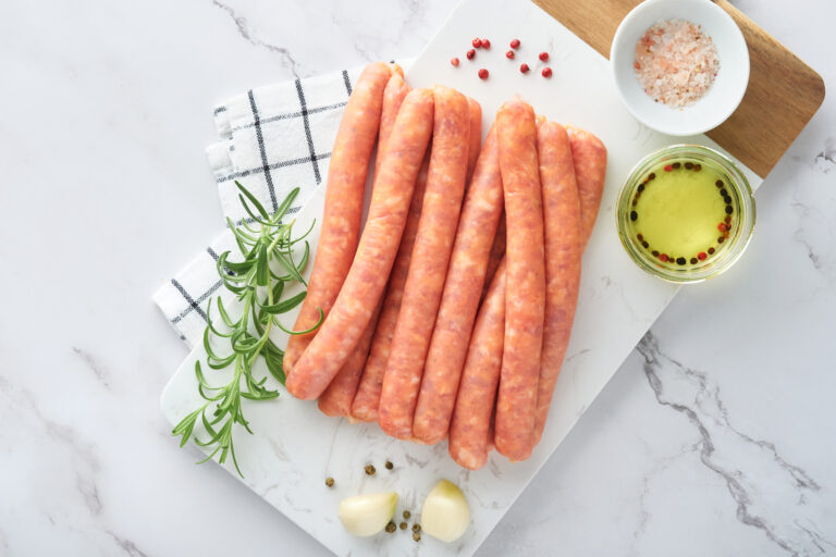 Meat beef sausages. Raw barbecue sausages with spices, vegetables and ingredients for cooking on white background. Top view. Copy space. Beer Fest menu concept.