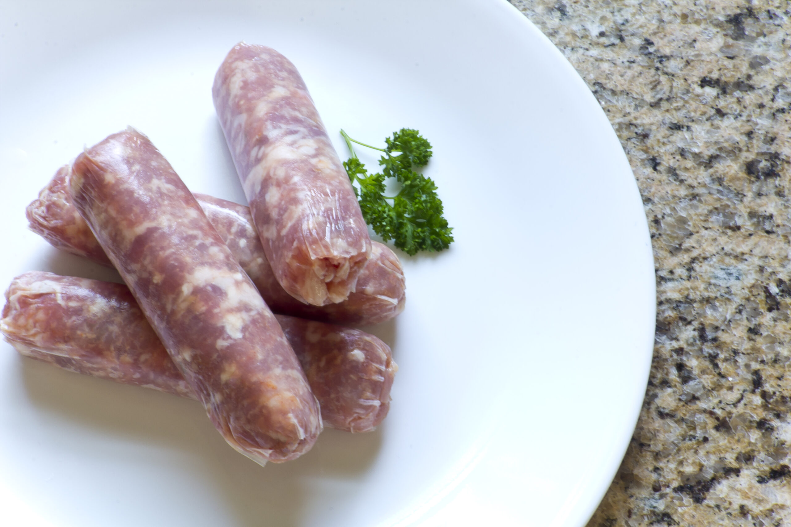 Raw Italian sausage on a white plate with parsley ready to cook