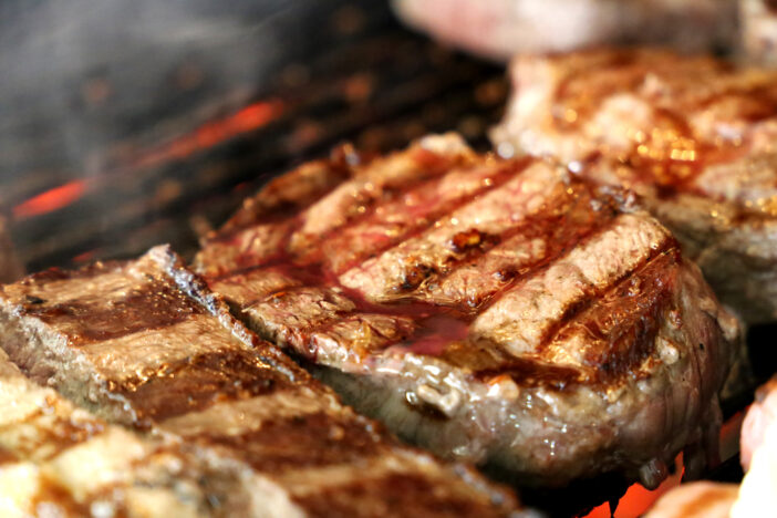 Ancho steak grilled on the grill with glowing charcoal in the background. Many steaks lined up. Side view.