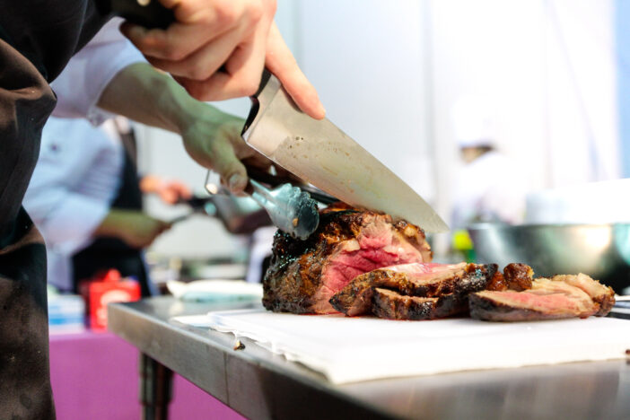 Chef with knife and cutting tasty grilled steak, Chef preparing food, meal, in the kitchen chef at work