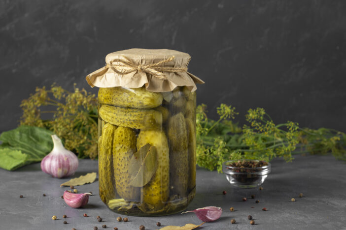 Homemade pickled cucumbers with garlic, horseradish, pepper and dill in glass jar on gray background