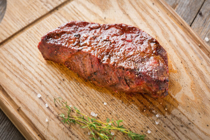 Hot Grilled Whole Denver Steak on Wooden Board with Herbs. Fresh Juicy Medium Rare Beef Grillsteak. Barbecue Meat Close Up