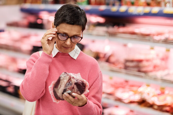 Waist up portrait of adult woman choosing fresh meat shopping for groceries in supermarket, copy space