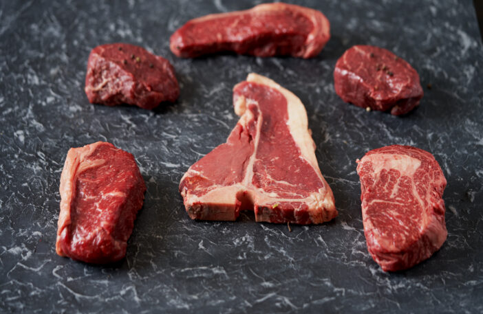 Cold cuts - raw, aged, juicy steaks of filet mignon, t-bone, ribeye, striploin, on a dark stone background. Top view, assortment of premium segment beef steaks